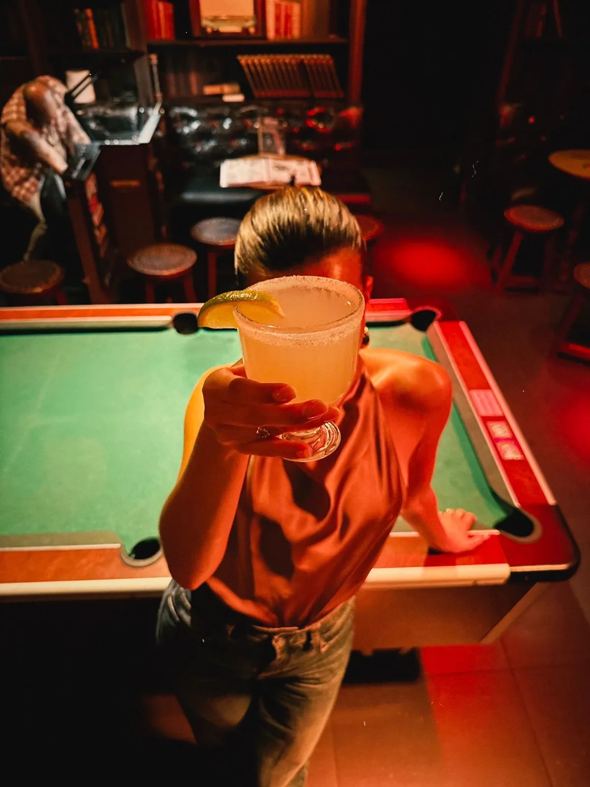 Une personne appuyée sur le billard vert, un cocktail à la main