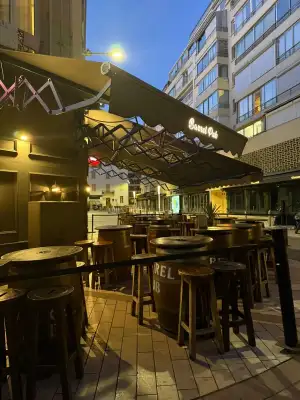 La terrasse couverte sous le store à la tombée de la nuit, ses tonneaux et ses tables hautes, vue depuis la rue